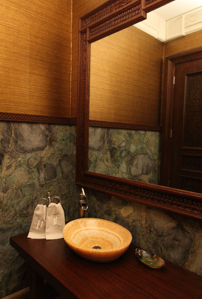 Un espejo tallado se luce en el baño de visitas. La pared está forrada con granito y una guarda en papel tapiz