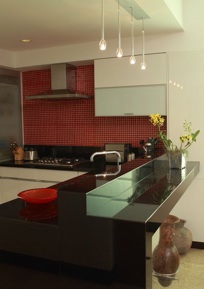 El diseñador Jorge Vallarino optó por hacer una cocina abierta, vista desde el área social.  En la pared de atrás se colocaron mosaicos de vidrio rojos para que contrasten con el granito negro y el blanco brillante de los anaqueles.