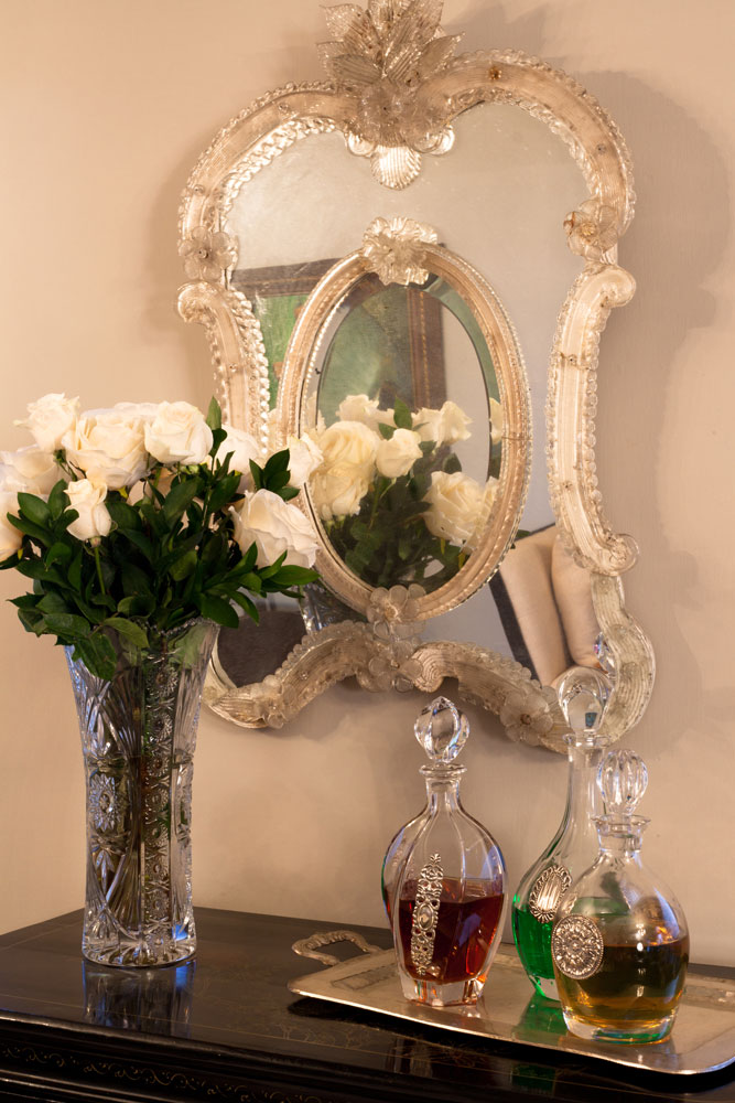 Mueble bar chino en el que se aprecian un espejo veneciano, florero de cristal tallado y botellas de cristal. 