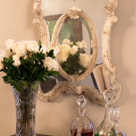 Mueble bar chino en el que se aprecian un espejo veneciano, florero de cristal tallado y botellas de cristal. 